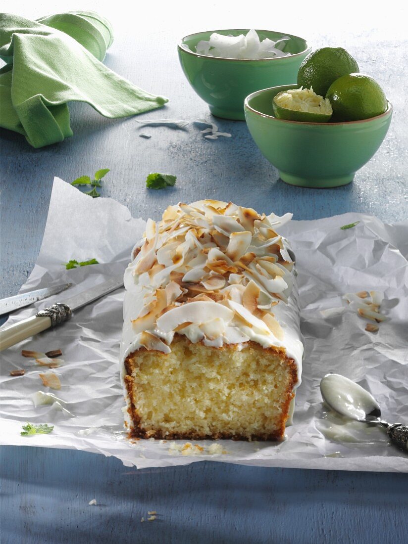 Limetten-Kokos-Kuchen, angeschnitten, auf Papier auf blauem Holztisch