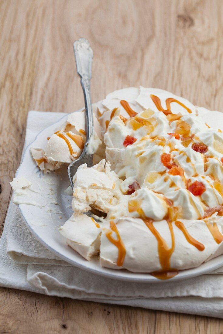 Pavlova with whipped cream, candied fruits and caramel sauce