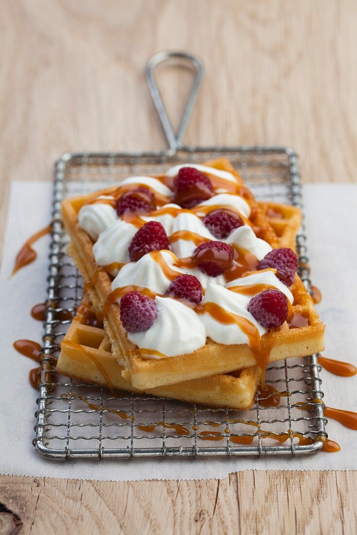 Waffles topped with cream, raspberries and caramel sauce