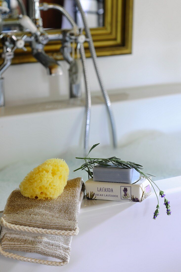 Toiletries, sponge and lavender soap on edge of bathtub