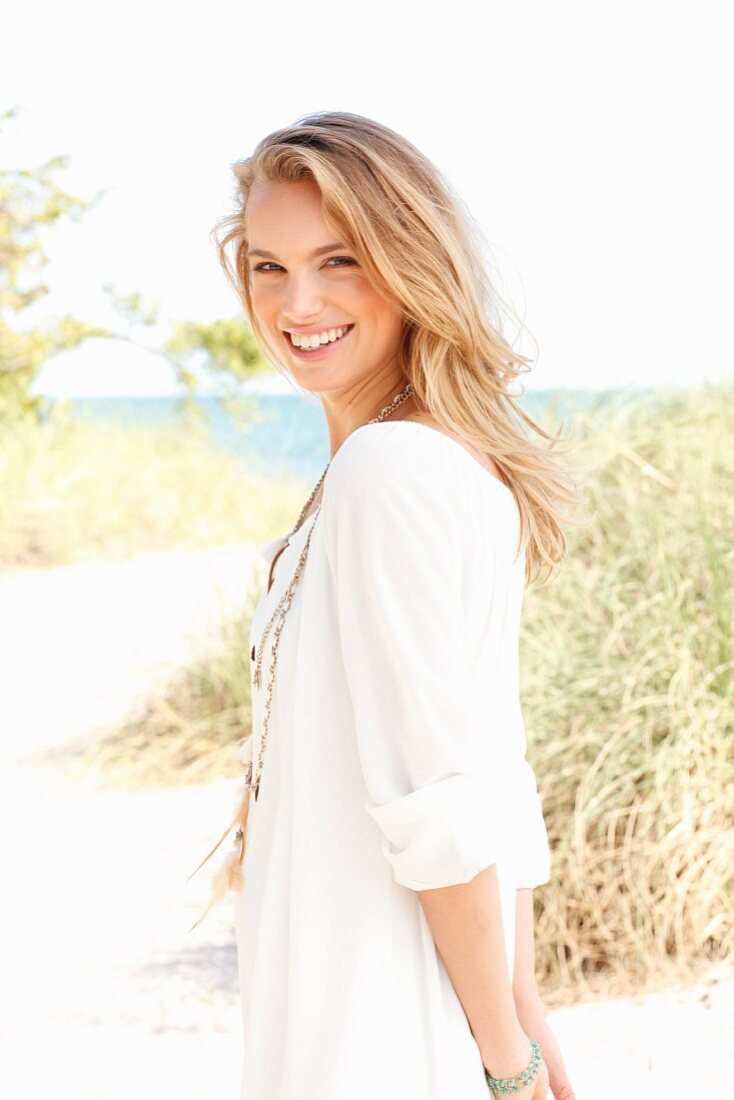 A young blonde woman on a beach wearing a white tunic