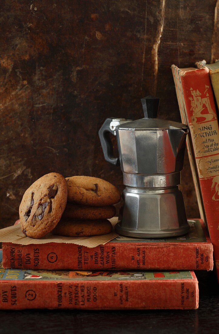 Chocolate chip cookies next to an espresso maker on a pile of old books