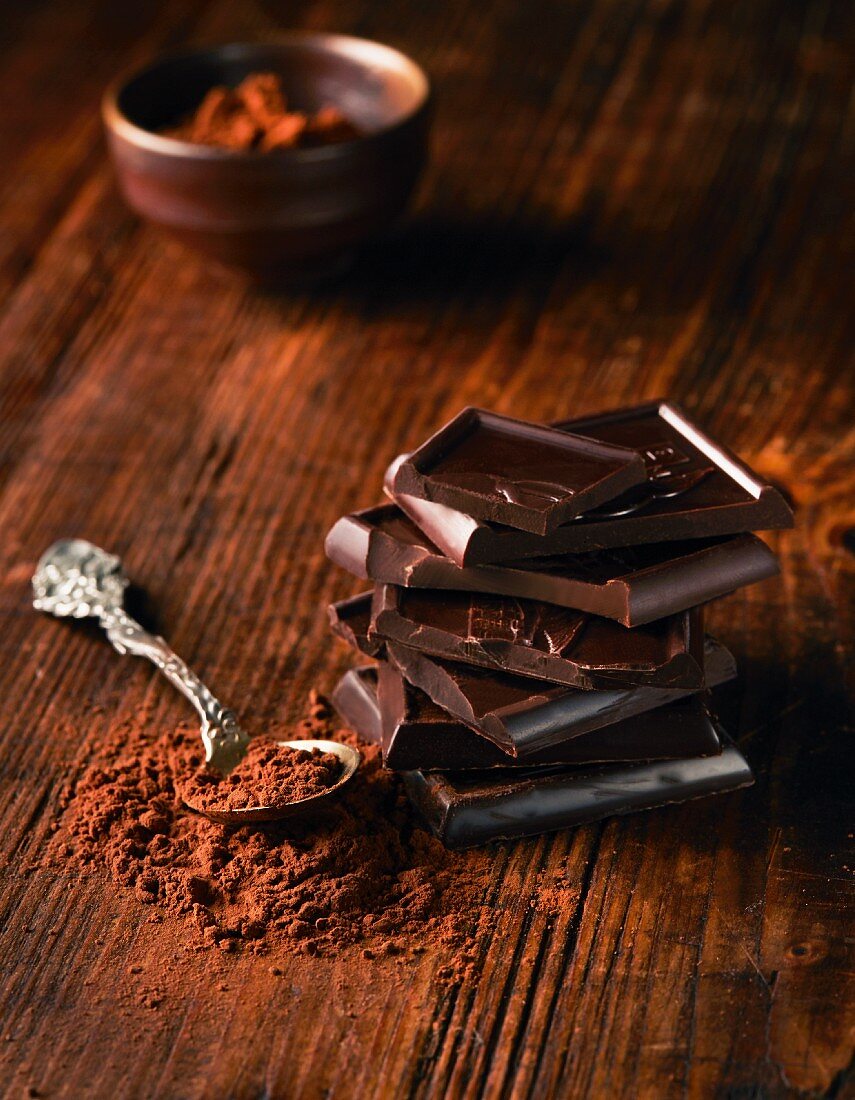 A stack of chocolate pieces next to a pile of cocoa powder