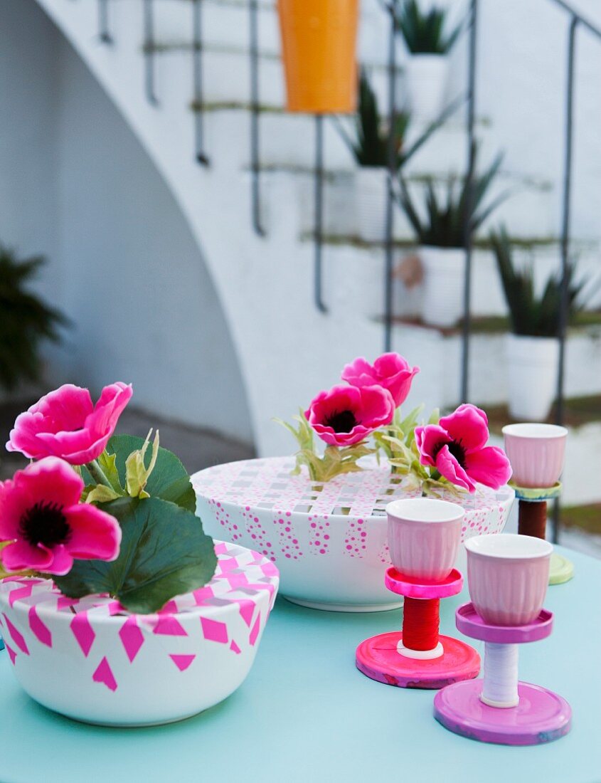 Colourful table decorations: bowls of anemones criss-crossed with washi tape and stands hand-made from jar lids and thread reels
