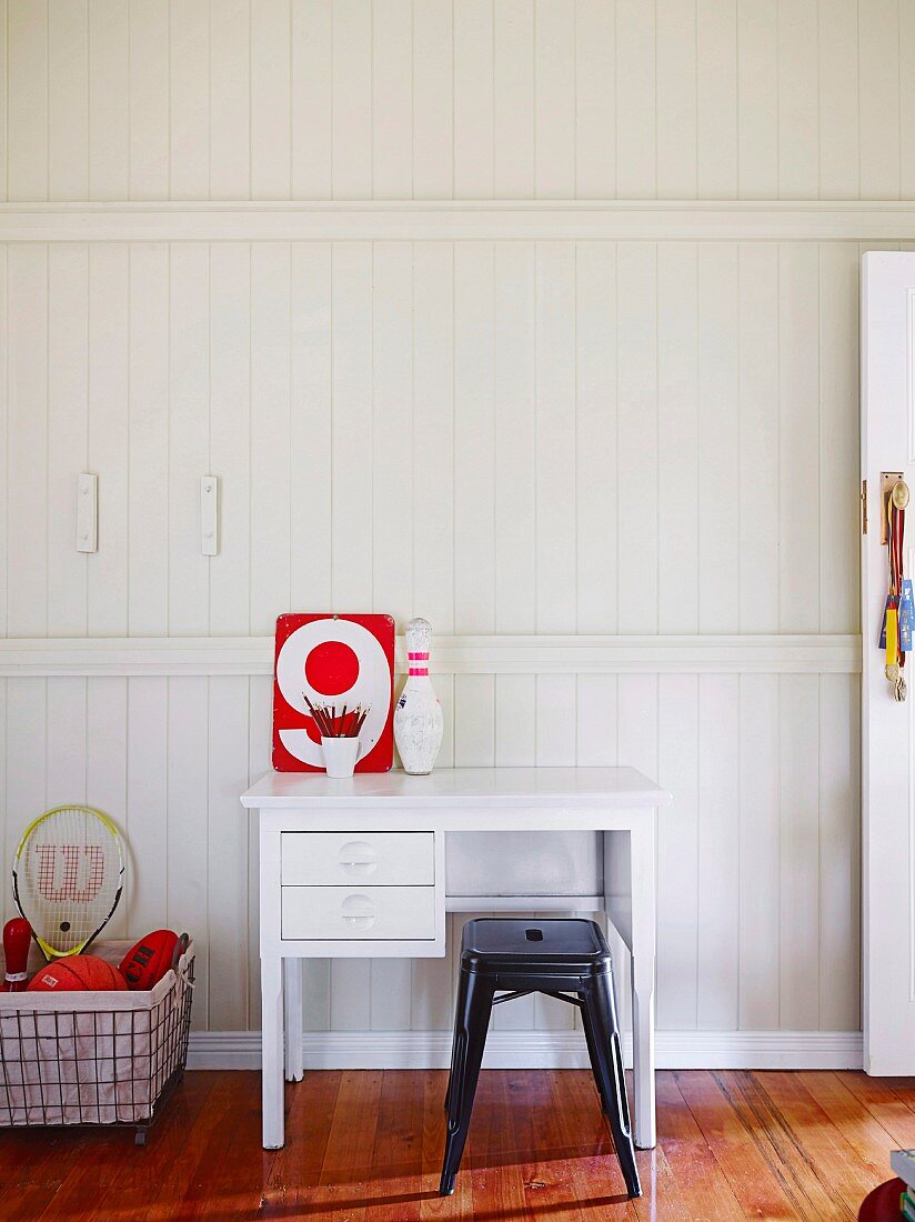 White desk and black classic metal stool against white wooden wall