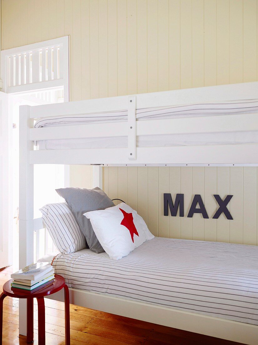 Red stool with a stack of books next to a white bunk bed on a wooden panel with decorative letters