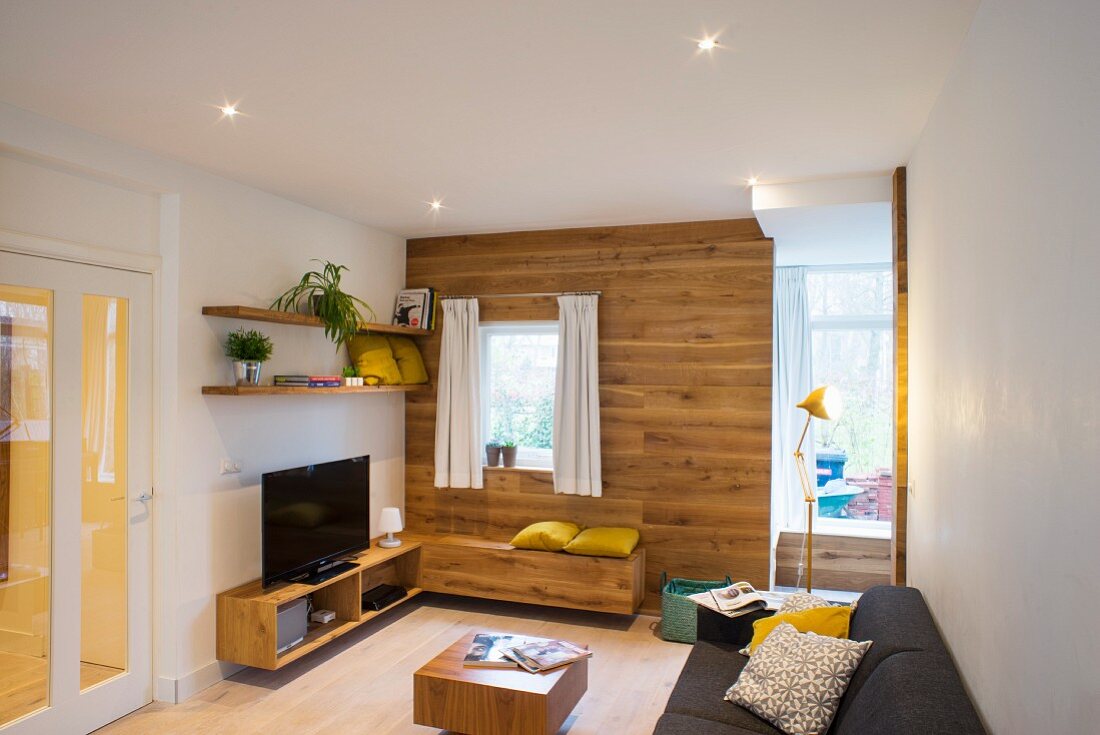 Lounge area with wood-clad wall and matching bench and sideboard next to open doorway