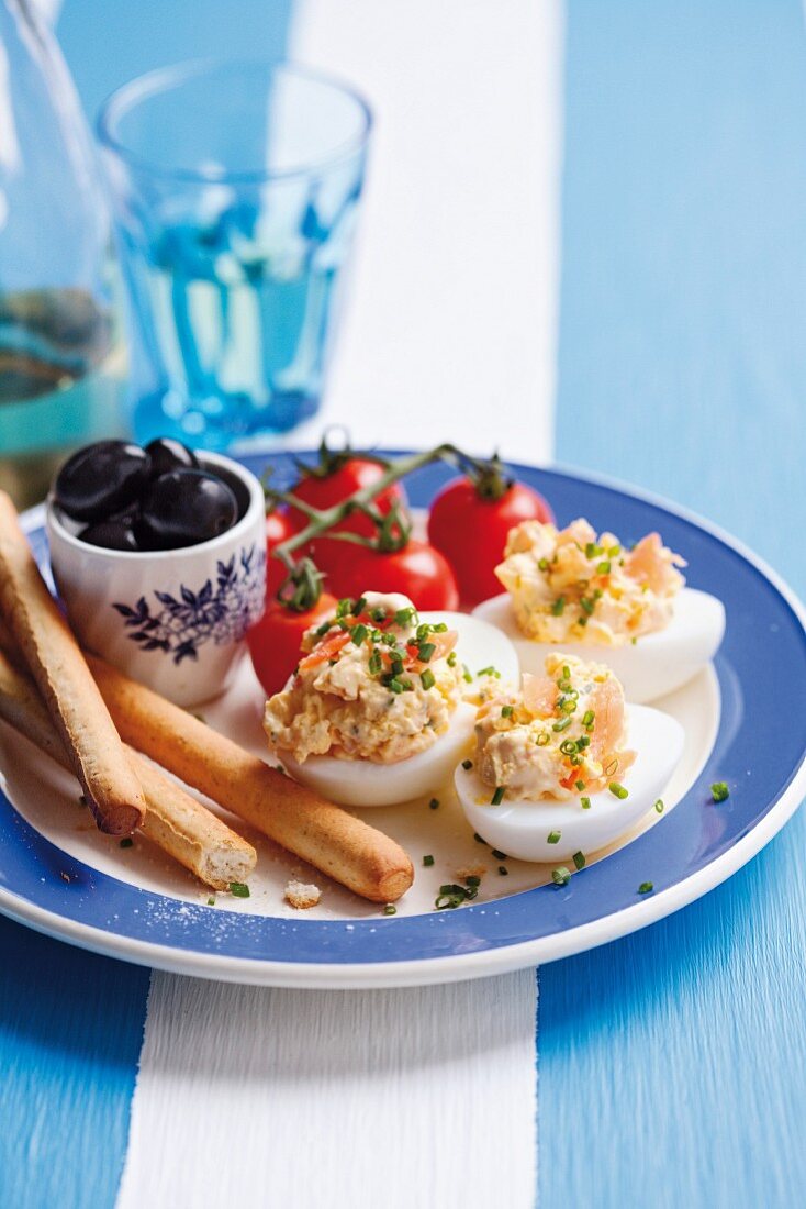 Devilled eggs filled with salmon trout served with olives, breadsticks and tomatoes