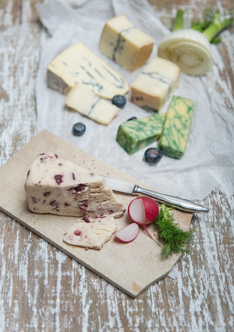 Wensleydale, Jacobean-Salbei, Cambozola, Morbier mit Fenchel, Radieschen und Heidelbeeren auf Holzbrett und Papier