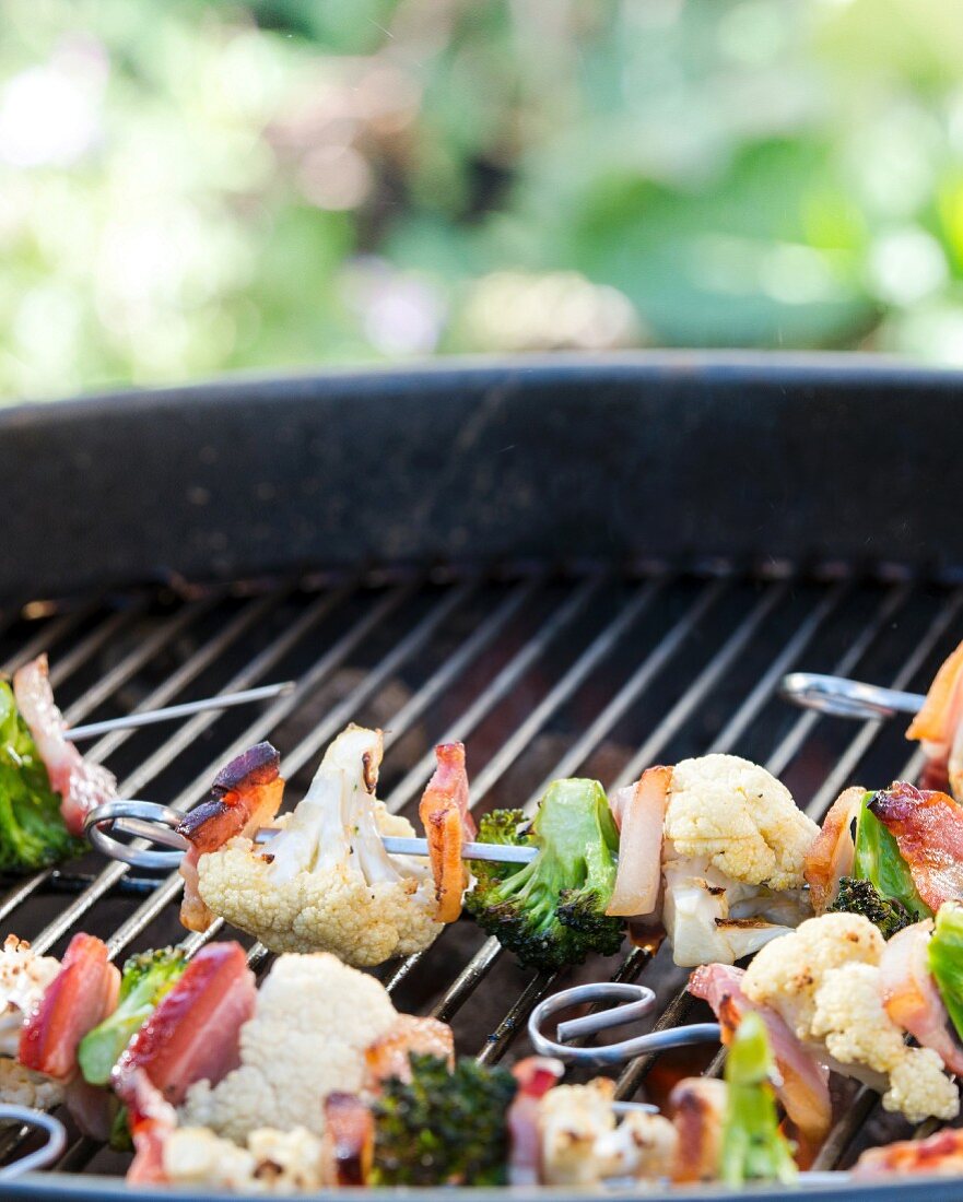 Cauliflower and broccoli skewers with bacon on a barbecue