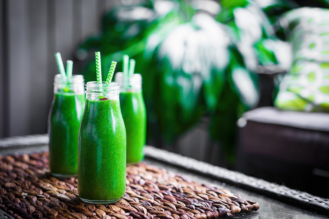 Frische grüne Smoothies in Glasflaschen mit Trinkhalm