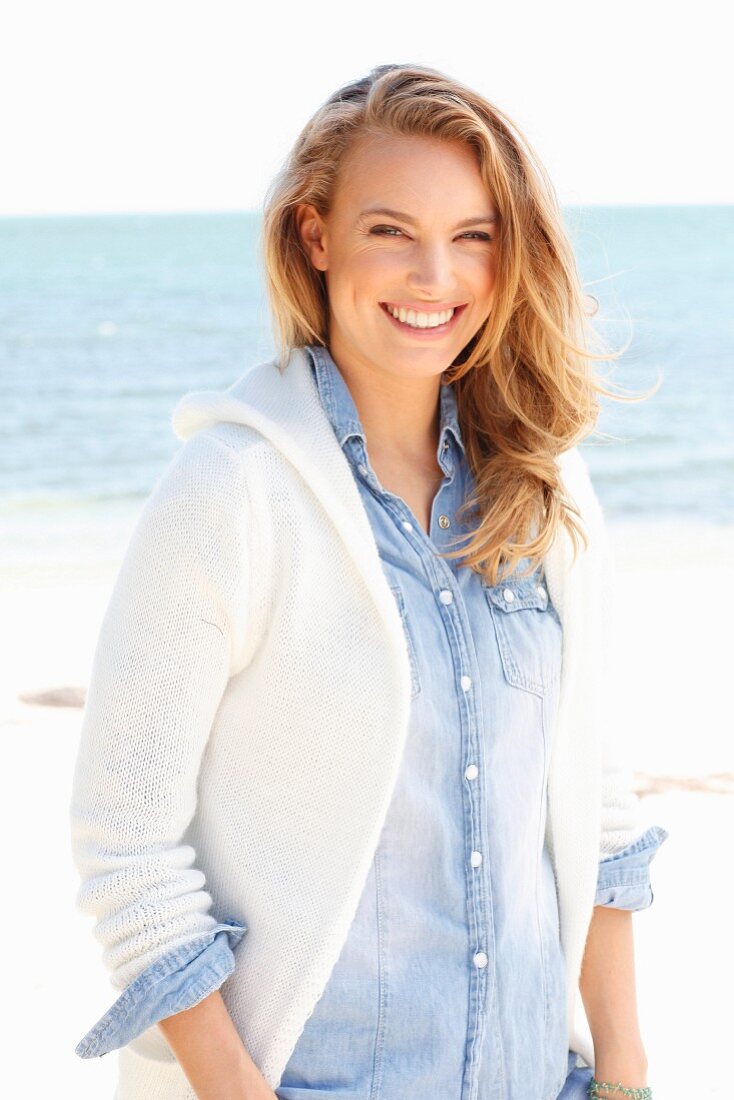 A young woman on a beach wearing a denim shirt and a cardigan