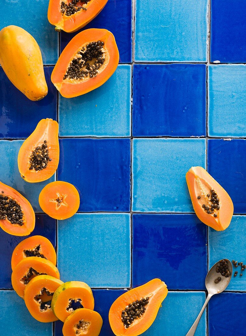 Frische Papayas, ganz und durchgeschnitten auf blauem Fliesenuntergrund