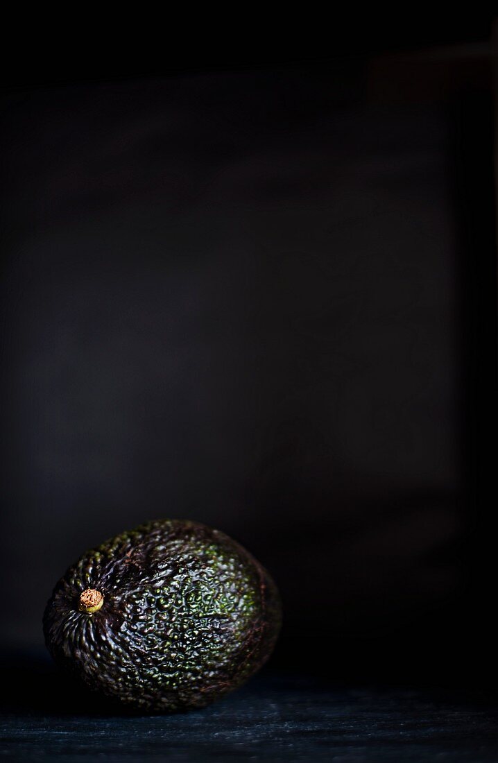 An avocado on a slate platter against a black background