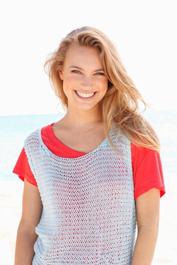 A blonde woman on a beach wearing a red top and a crocheted top