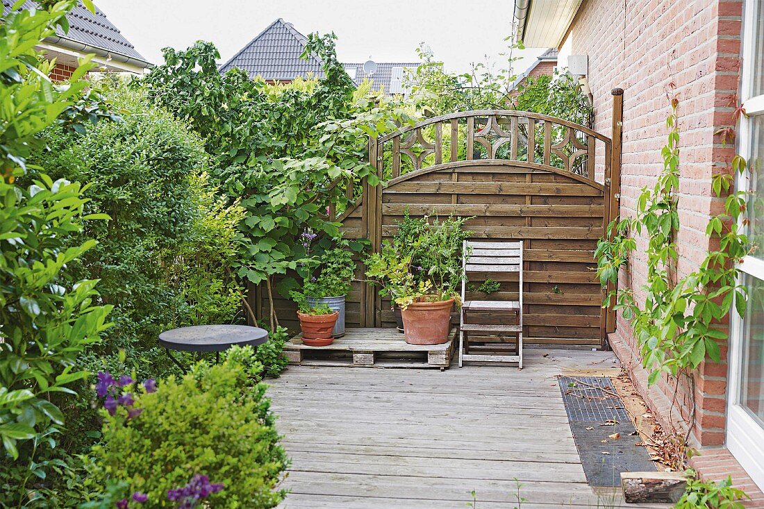 A wooden terrace with green plants and a privacy fence