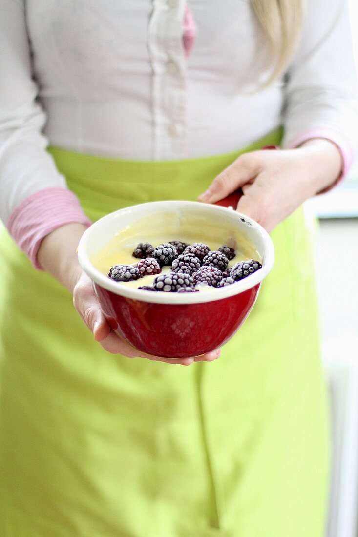 A woman holding a bowl of pudding and blackberries