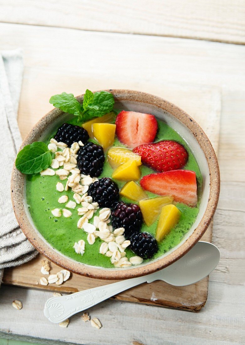 A smoothie bowl made with cabbage, apple and kiwi garnished with strawberries, peaches, blueberries and oats