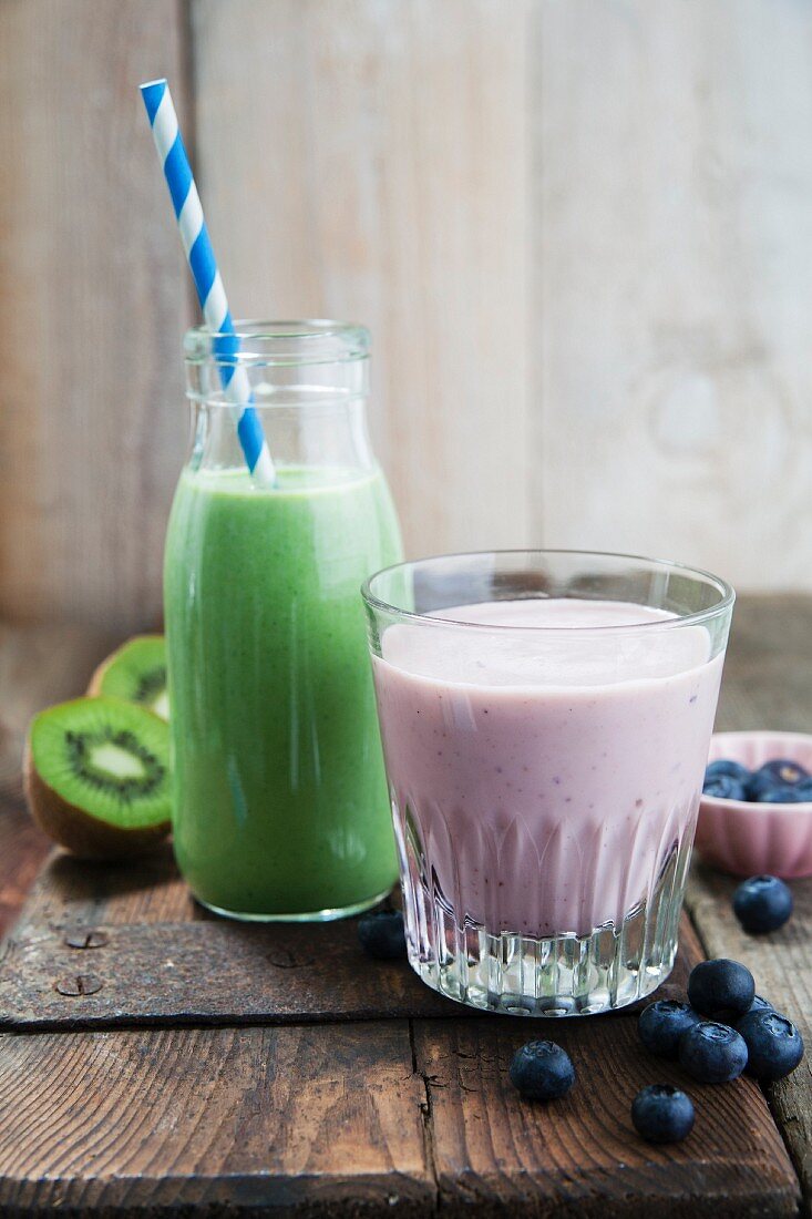 A kale and apple smoothie in a glass bottle and a blueberry and banana smoothie in a glass
