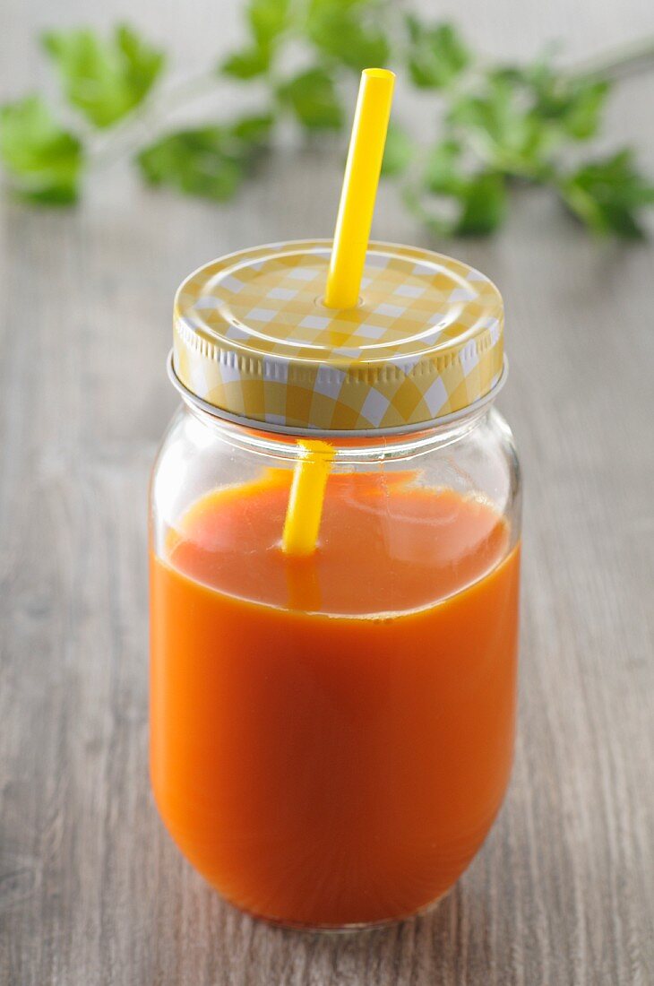 Carrot juice in a screw-top jar with a straw