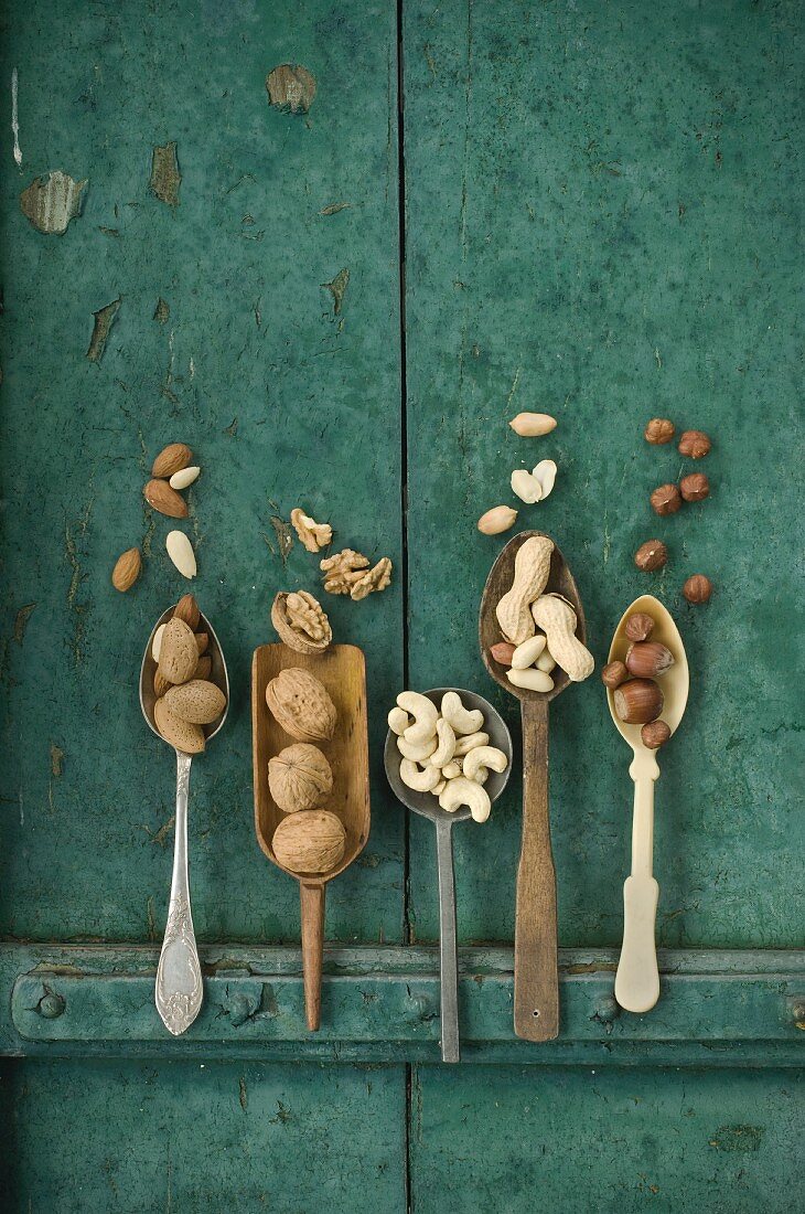 Various nuts: walnuts, hazelnuts, almonds, peanuts, cashew nuts and macadamia nuts on a wooden surface on spoons