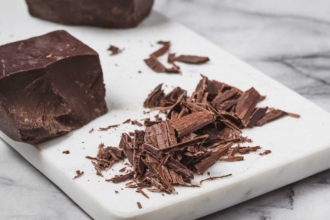 A chunk of chocolate and grated dark chocolate and a marble surface