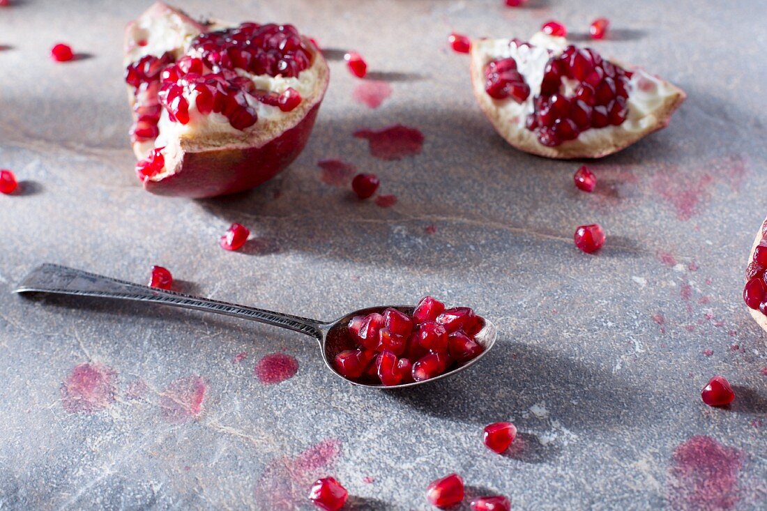 Sliced pomegranates and a spoon of pomegranate seeds