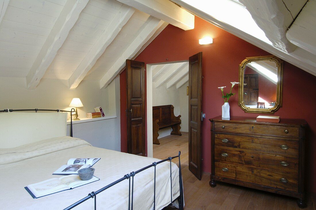 Antique chest of drawers and red wall in attic bedroom