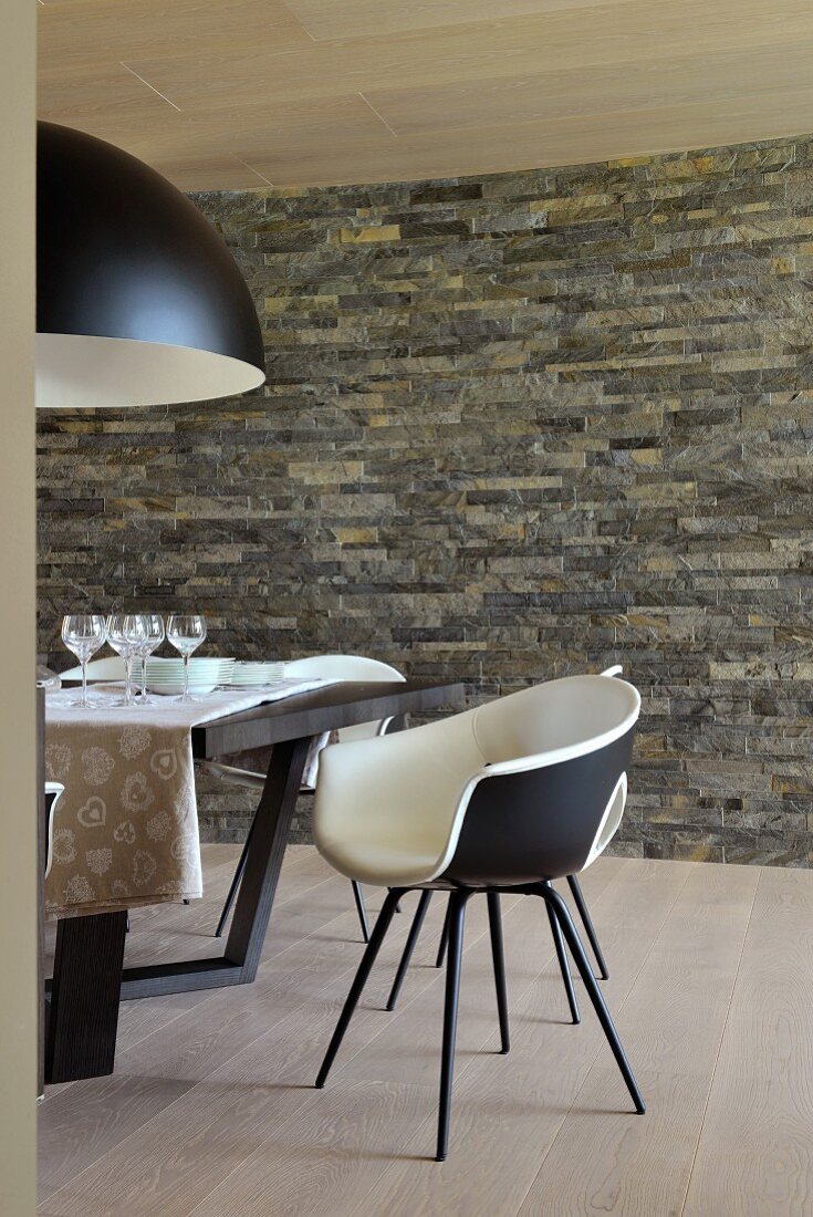 Essbereich mit Natursteinwand, schwarz-weisser Retro Schalenstuhl am Tisch