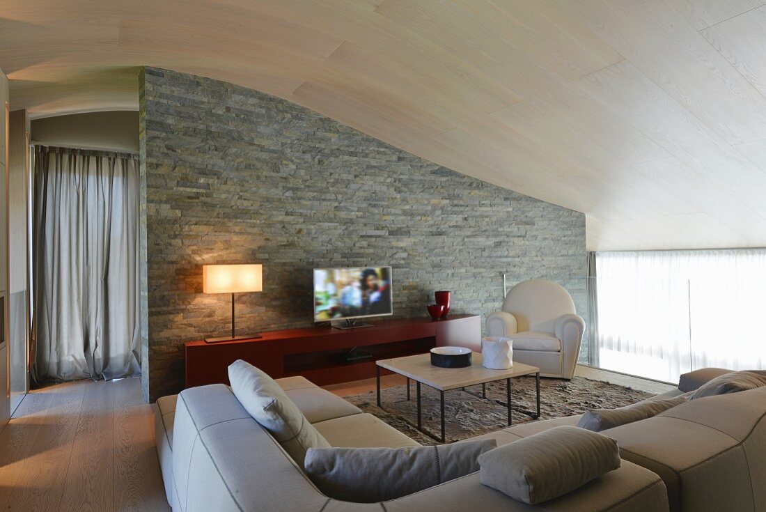 Elegante Lounge unter geschwungener Decke, im Hintergrund Natursteinwand
