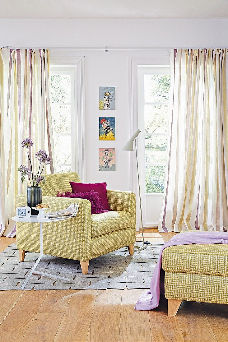 An upholstered armchair and a pepita-patterned footstool against striped curtains in a living room in lilac and delicate green