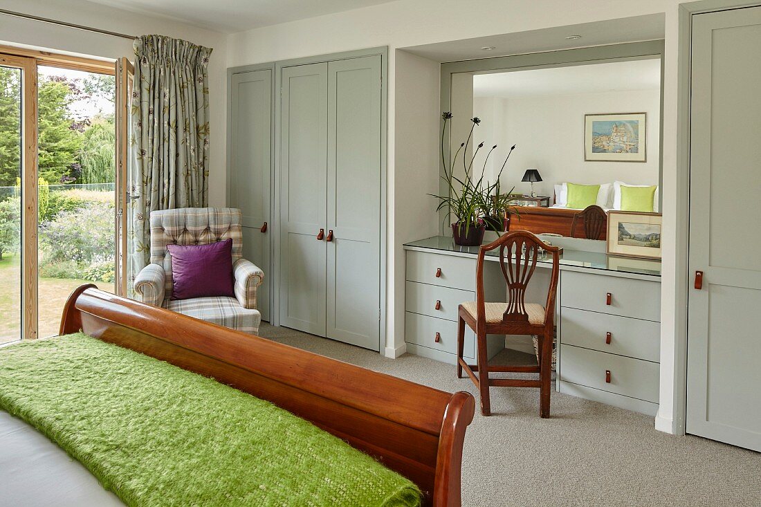 Wooden sleigh bed and pale grey fitted wardrobes with integrated dressing table in bedroom