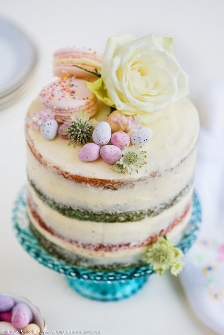 Vierschichtiger Ombre Cake mit weißem Zuckerguss, Macarons, Ostereiern und Blumendeko
