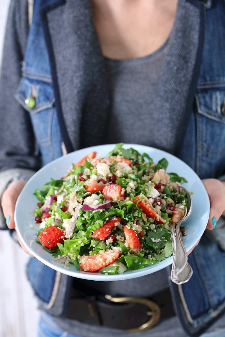 A plate of spinach and quinoa salad with strawberries and pomegranate seeds