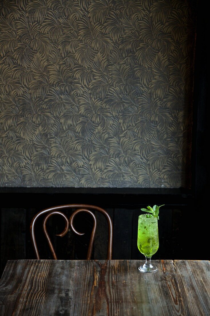 A Mojito on a wooden table against a wall with artistic wallpaper