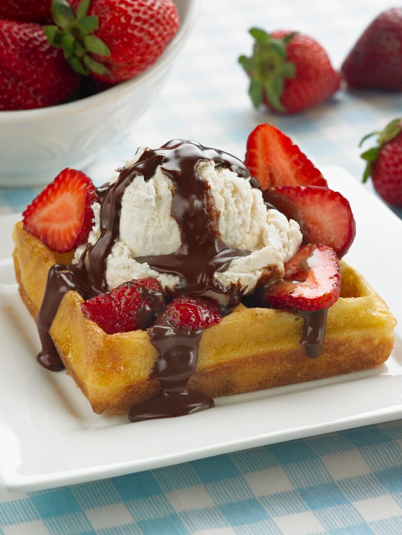 A waffle topped with strawberries, vanilla ice cream and chocolate sauce