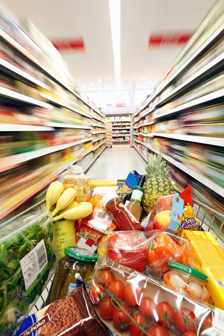 Einkaufswagen voller Lebensmittel zwischen Regalen in Supermarkt