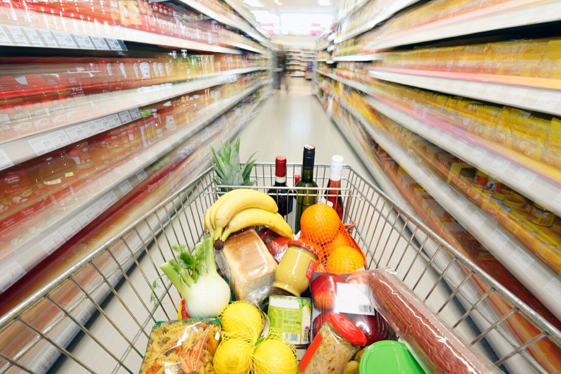 Einkaufswagen voller Lebensmittel zwischen Regalen in Supermarkt