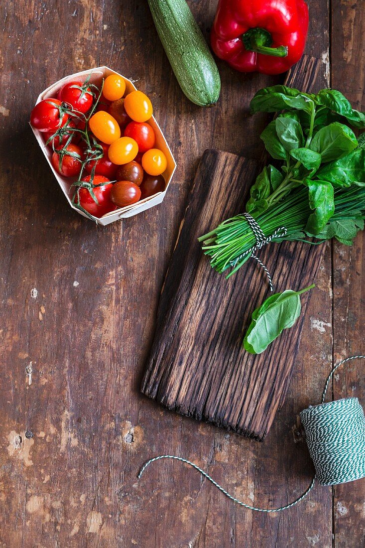 Tomaten, Zucchini, Paprika und Kräutersträusschen auf rustikalem Holztisch
