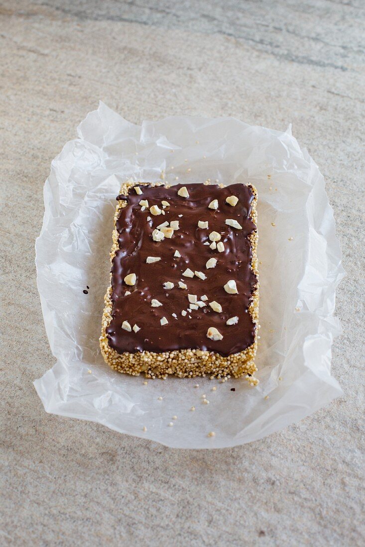 An amaranth bar covered with chocolate and cashew nuts on a piece of paper