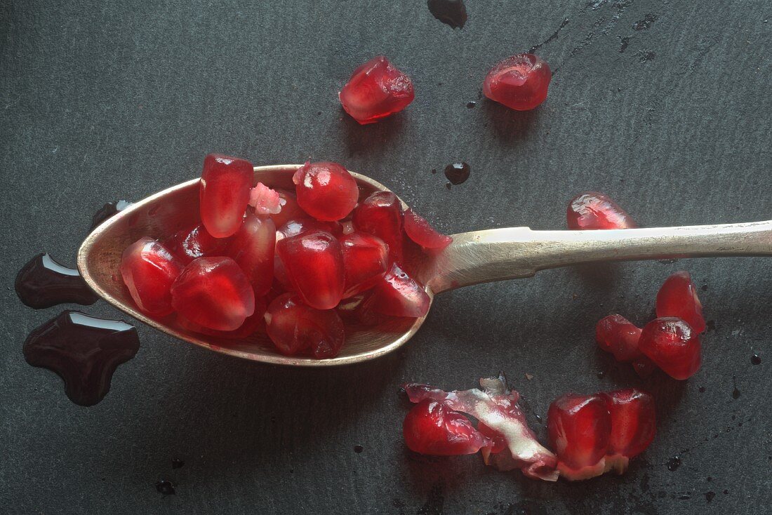 A spoonful of pomegranate seeds on a slate surface