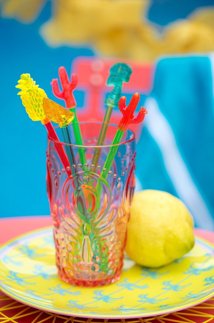 Colourful swizzle sticks in plastic beaker on plate