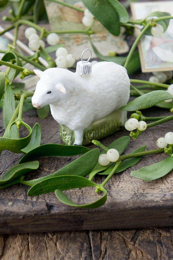 Sheep Christmas-tree bauble amongst sprigs of mistletoe on wooden surface