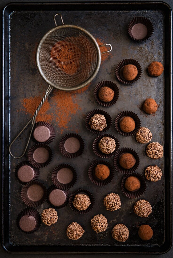 Various chocolate truffles with a sieve and cocoa powder on a baking tray