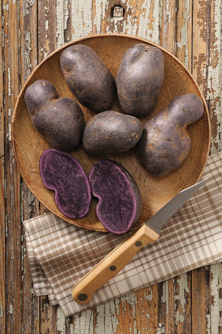 Blaue Kartoffeln mit Messer auf Holzteller