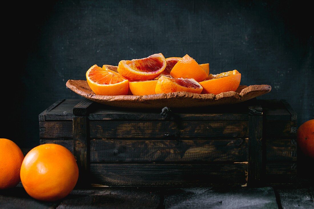 Wedges of Sicilian blood oranges on a plate and in a wooden crate