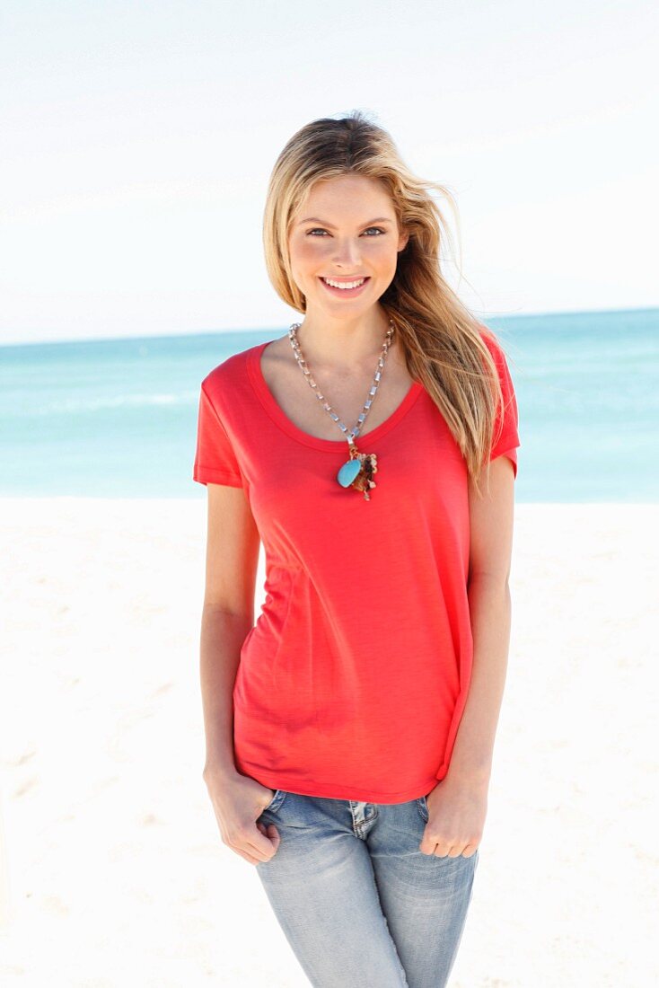 A young woman on a beach wearing a red top and jeans