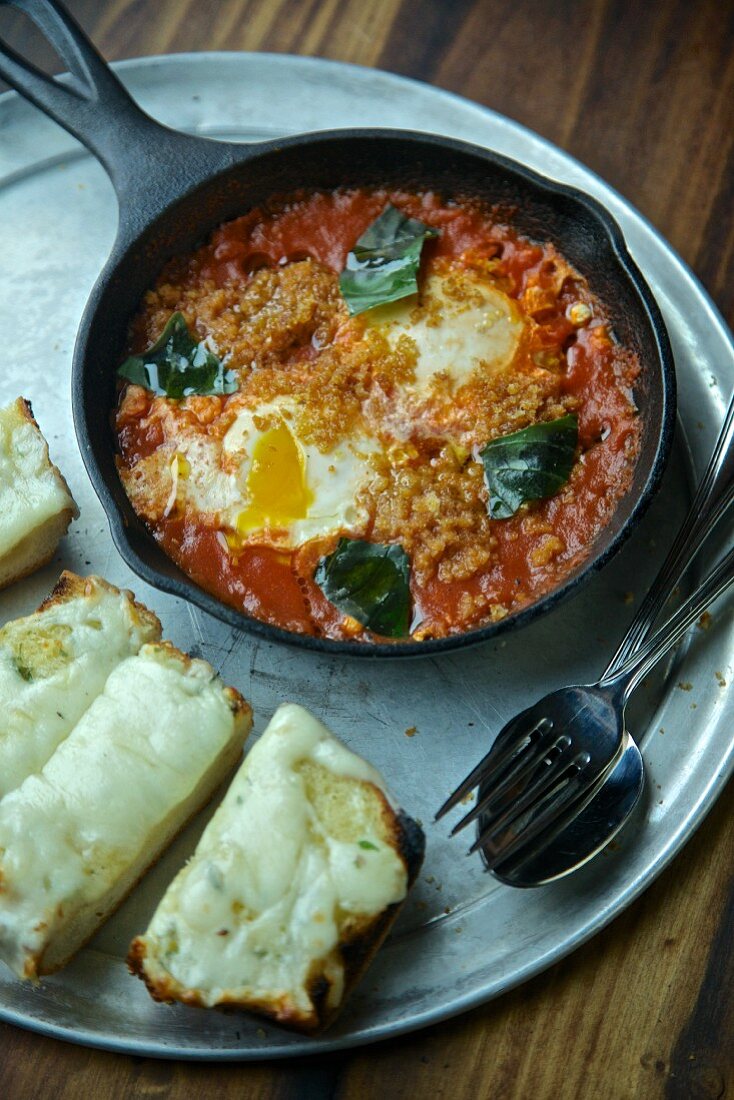Eggs with tomatoes and basil in a pan served with cheese on toast
