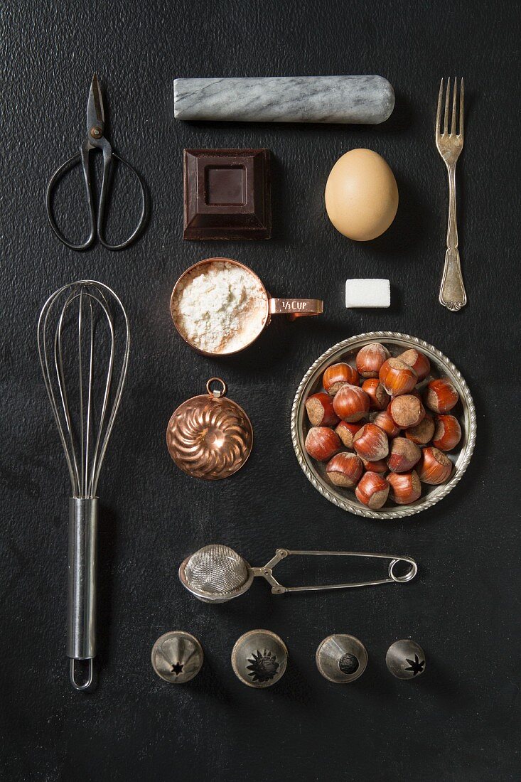 An arrangement of kitchen utensils and baking ingredients on a dark surface