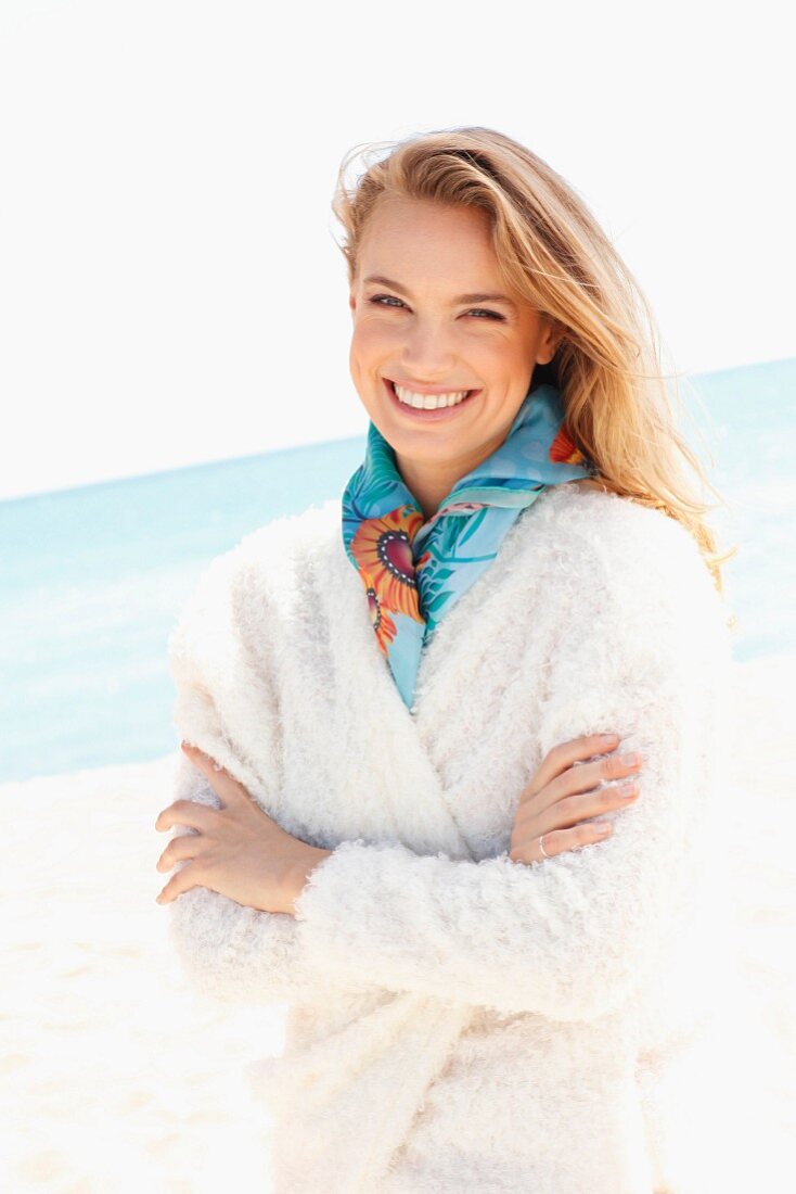 A young woman on a beach wearing a fluffy white jacket